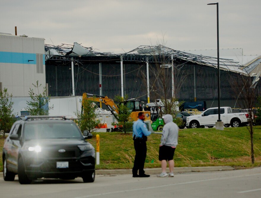 A police officer talks with a bystander infront of a partially destroyed Amazon warehouse.