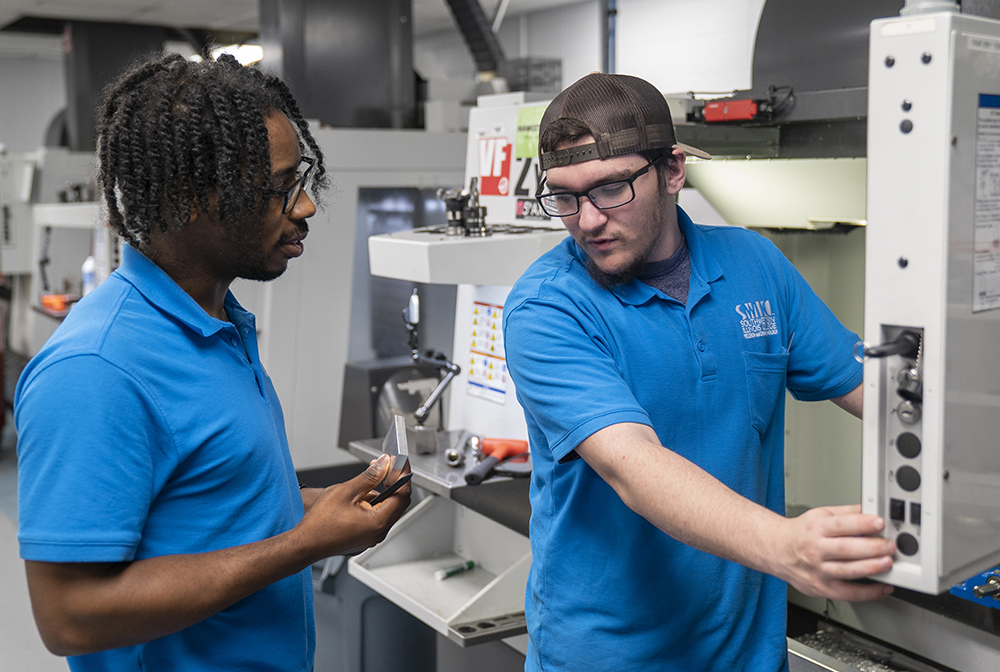 Two students discuss how to machine a metal piece.